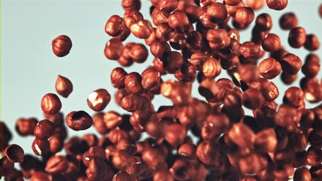 Peeled hazelnuts fly up and fall down. On a blue background. Filmed is slow motion 1000 fps.