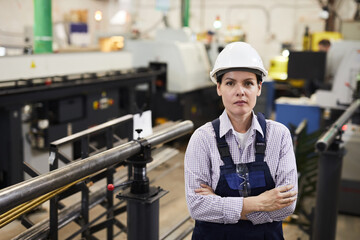 Portrait of serious confident experienced female worker of large metalworking production standing in industrial workshop and crossing arms on chest