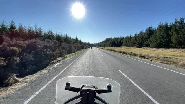 POV Motorcycle ride on a rural paved road on a sunny blue sky day with a big sun in the shot