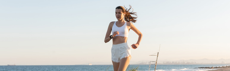 young woman in shorts and wireless earphone jogging near sea, banner.