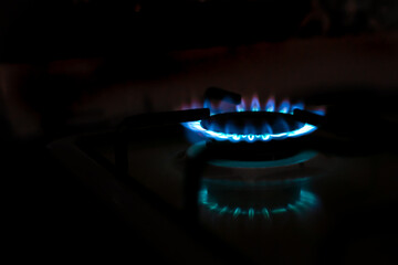 Gas stove burner with blue flame with reflection in the dark, copy space, blurred background. gas crisis.