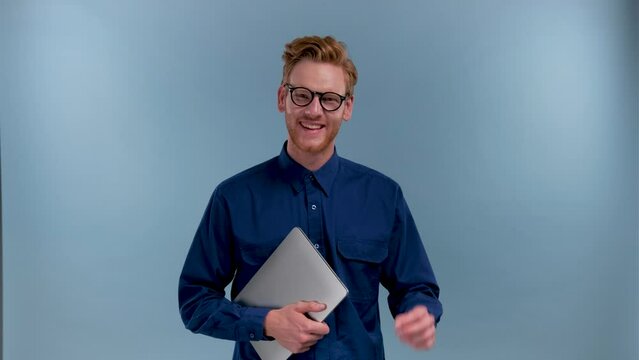 portrait of smiling young IT specialist with laptop in blue studio
