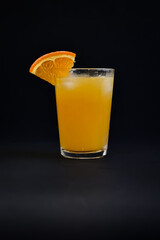 Photo of a glass of cold orange juice with a piece of orange as a decoration on a black background