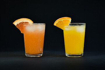 Photo of a glass of orange juice and a glass of grape fruit juice on a black background