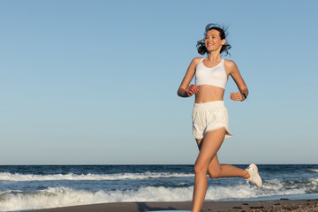 cheerful young and sportive woman jogging near sea in summer.
