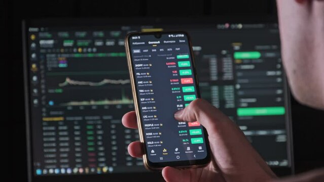 Investor checking cryptocurrency price on smartphone screen. Many crypto assets show growth. Green portfolio. Stock charts of the exchange rate. Businessman analyzing digital stock market investments