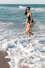 Fototapeta na wymiar cheerful woman in black swimsuit and stylish sunglasses standing in sea.