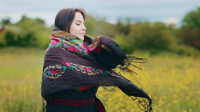 Young stylish woman attractive girl spend time alone outdoors wears ukrainian traditional dress black clothes hold up fluttering patterned colorful shawl stand on field grass wrap in fashionable scarf