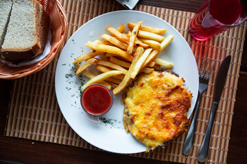 Appetizing French style meat topped with Mornay cheese sauce served with fries and ketchup. Festive Russian cuisine.