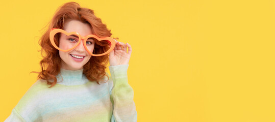 happy redhead woman wear funny party glasses on yellow background, celebration. Woman isolated face portrait, banner with copy space.
