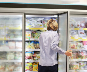 Fototapeta na wymiar Man choosing frozen food from a supermarket freezer... choosing a dairy products at supermarket, reading product information