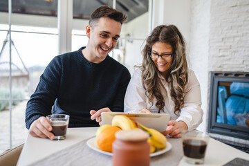 Couple female and male caucasian sitting in a living room drinking coffee and looking at their tablet shopping online Technology and modern lifestyle concept