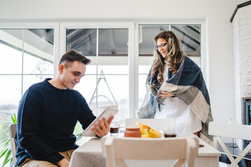 Obraz premium Couple female and male caucasian sitting in a living room drinking coffee and looking at their tablet shopping online Technology and modern lifestyle concept