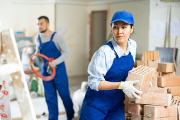 Skilled asian female builder in blue workwear planning erection of partition wall in building under...