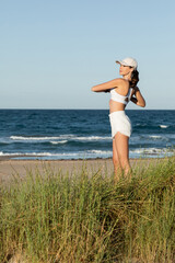 young fit woman in shorts and sports bra exercising near blue sea on beach.