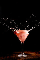 Splash shot with martini cocktail foam with cherry on wooden counter with dark background