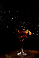 Splash shot with orange martini cocktail drink on wooden counter with dark background