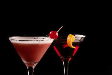Two martini glasses with close up on cherry cocktails and red liquid and orange shavings