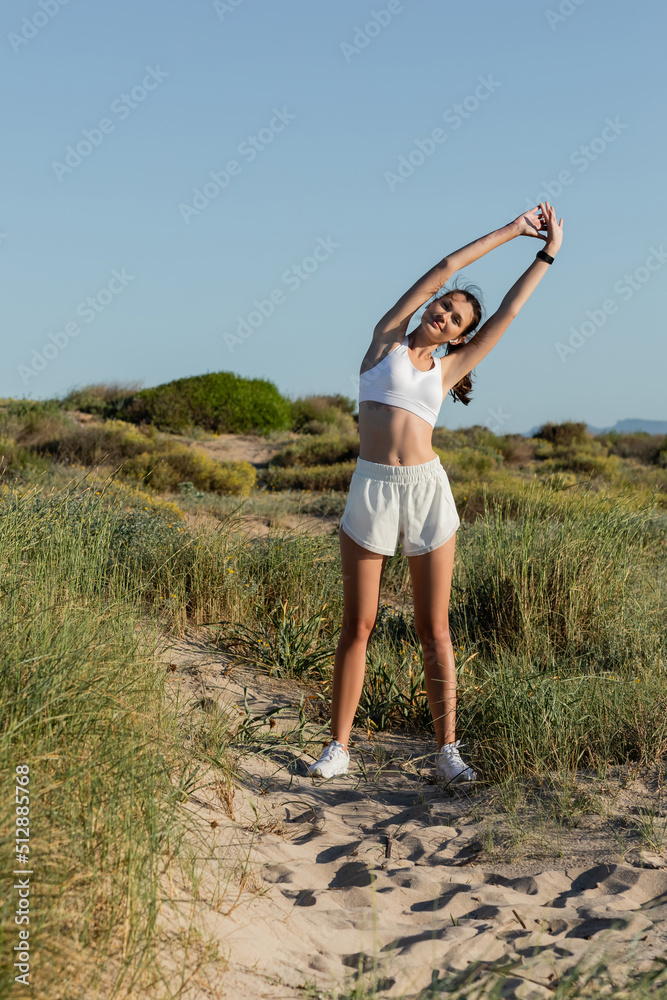 Wall mural happy fit woman in wireless earphones and sportswear stretching outside.