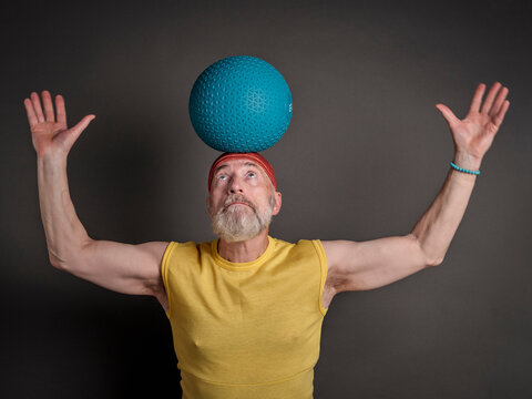 senior man is balancing a heavy slam ball on his head, fit over 60 concept