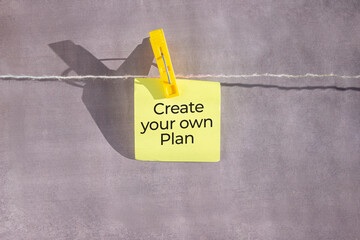 Create your own Plan text on a yellow sticker on a rope with clothespins on a grey background.