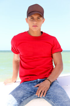young man with red t-shirt and brown cap, on the beach. summer concept. 