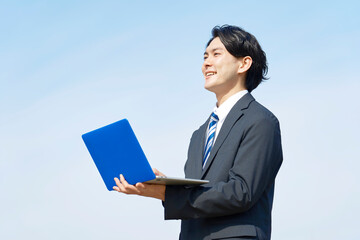 青空背景でノートパソコンを使うビジネスマン