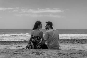 pareja sentada mirándose frente a frente, y el mar de fondo en palomino