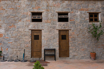 Fototapeta na wymiar front facade of a medieval house with two wooden doors and two old windows above at a brick and rock stone wall in a medieval italian tuscany villa in Val'Quirico, Tlaxcala, Puebla, Mexico