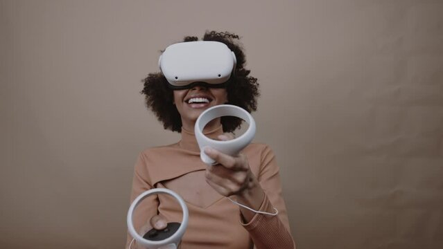 Shot of Latin young woman standing with VR goggles and keep joysticks or finger as a gun. Cinematic 4K