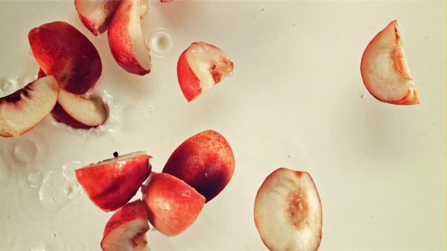 Pieces of fresh peach fall into the milk with splashes. Macro background. Top view. Filmed on a high-speed camera at 1000 fps.