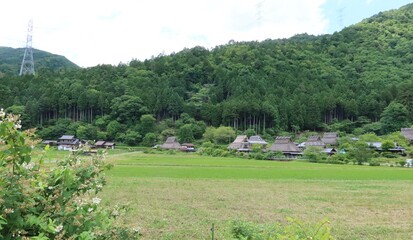 A scene of Japanese traditional houses with a thatched roof in the preserved area of them and Yura-gawa River in Miyama Town in Nantan City in Kyoto Prefecture in Japan 日本の京都f府南丹市美山町にある萱葺の家々保存地区の風景