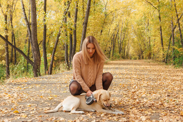 A young woman walking with her beloved labrador dog in autumn park.