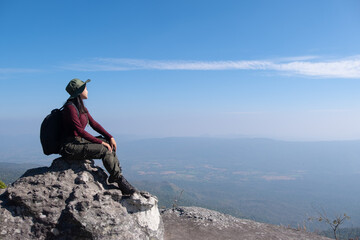 A traveler sits on a rock on a high mountain with a beautiful view of the sky.