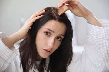 Young woman with problem of dandruff combing hair in bathroom - obrazy, fototapety, plakaty