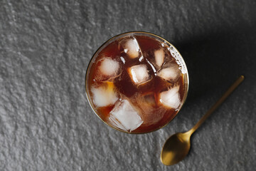 Glass of cold brew coffee with milk and spoon on dark background