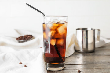 Glass of cold brew with straw on wooden table against light background