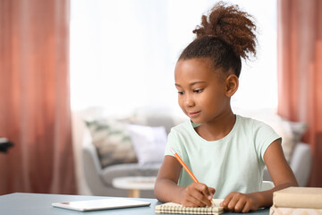 Little African-American girl writing in notebook at home