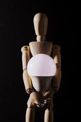 wooden mannequin holding a bulb isolated with black background