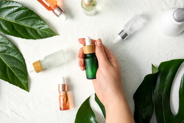 Female hand with different bottles of natural serum and plant leaves on light background