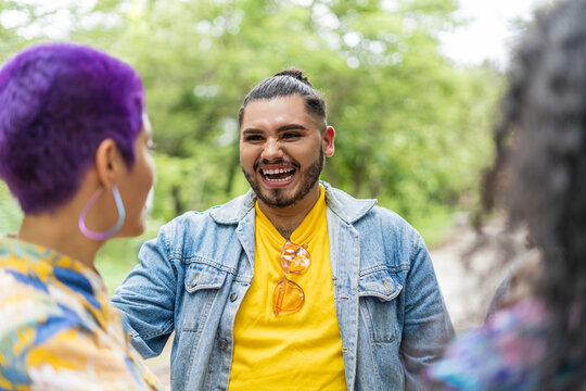 Hombre latino homosexual riéndose con sus amigas de la comunidad lgbt, mujer con cabello corto y pintado de morado en exterior