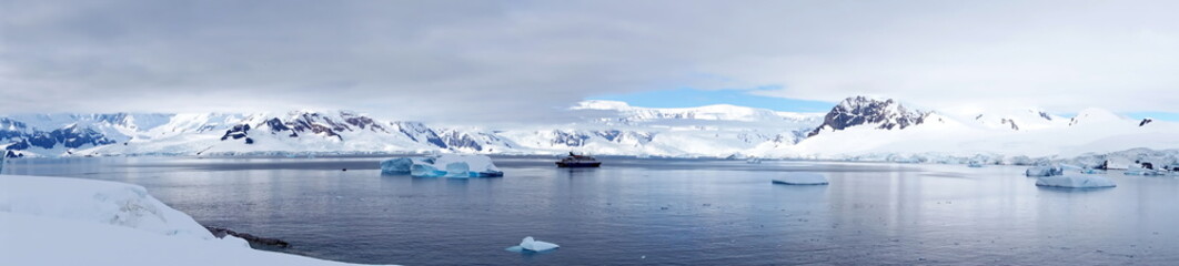 Panorama of an expedition cruise ship in a bay, surrounded by icebergs, at Portal Point, Antarctica - obrazy, fototapety, plakaty