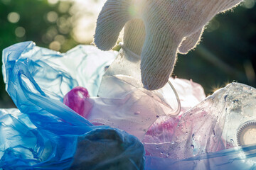 Plastic pollution in the environmental problem of the world. A hand in a white glove puts garbage in a plastic bag. Removal and cleaning of garbage from contaminated territories