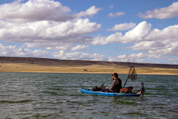 Fototapeta na wymiar Kayaker Wearing Life Jacket Fishing on Kayak with Trolley Motor and Fishing Poles and Net in Lake Hattie near Laramie Wyoming