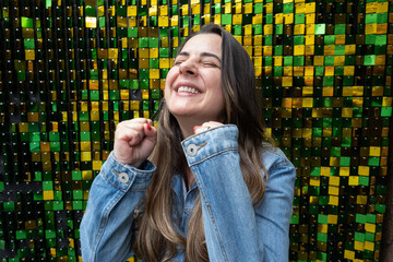 Brazilian woman celebrating with her hands on a background of Brazil colors with glitter