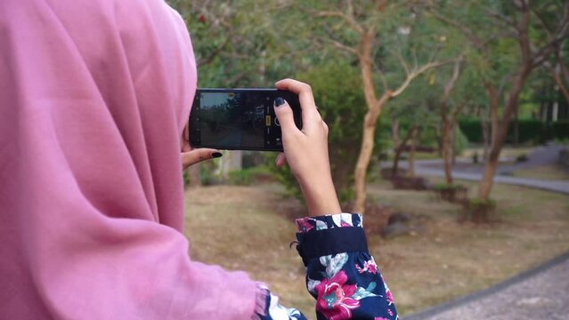 An Asian Muslim woman shoots some photos with a smartphone camera. Indonesian Muslim woman style with the smartphone.