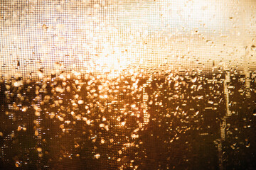 Close-up of raindrops on transparent glass.Blurred background of silhouette landscape, the sun with golden light during sunset or sunrise.The texture of wet glass. Abstract background.