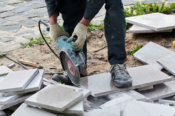 A worker with a circular saw cuts a tile in close-up.