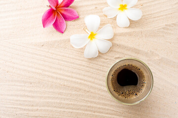 Black Coffee In Double Wall Glass On sand Beach Next To Frangipani Flowers.