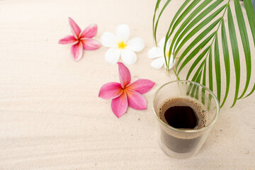 Obraz na płótnie Canvas Cup Lungo Coffee On Sand Beach Next To Frangipani flowers.